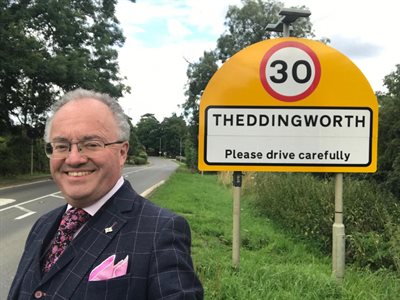 Commissioner in front of village 30mph sign