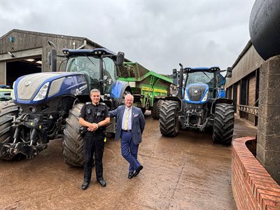 Police officer and PCC standing in front of tractors in a farm yard